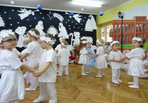 Dzieci w parach, ubrane na biało z opaskami na głowach wykonuja taniec Gwiazdeczek.